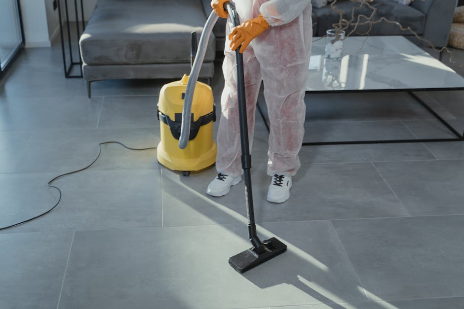 A person wearing orange cleaning gloves placing a lightbox sign with black letters spelling 'CLEANING HOME' on a table, in a bright indoor setting. The lightbox is illuminated with a warm glow, and th